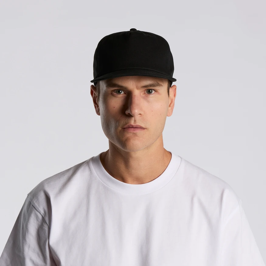 1119_SURF_COTTON_CAP_TURN__49216 Portrait of a man in a white T-shirt and black baseball cap, facing the camera against a light gray background.