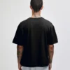 Back view of a person wearing a black oversized T-shirt and gray shorts, with tattoos on the neck and arms visible.