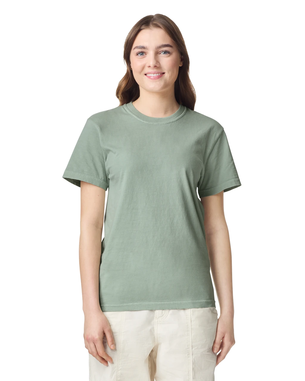 Smiling young woman wearing a sage green T-shirt and beige pants, standing against a white background.
