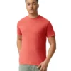 Young man in a coral T-shirt and light green/gray pants standing with one hand in his pocket against a white background.