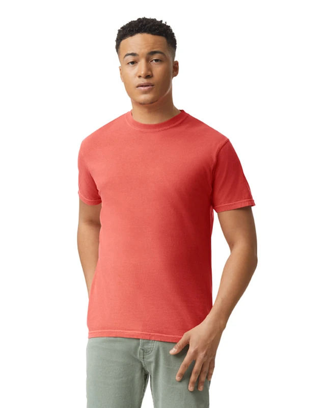 Young man in a coral T-shirt and light green/gray pants standing with one hand in his pocket against a white background.