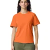 Woman in orange T-shirt and olive green pants standing against a white background, facing the camera.