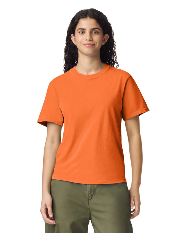 Woman in orange T-shirt and olive green pants standing against a white background, facing the camera.