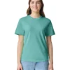 Woman wearing a teal crew-neck T-shirt and light-blue jeans, smiling at the camera against a white background.