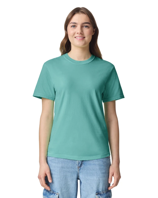 Woman wearing a teal crew-neck T-shirt and light-blue jeans, smiling at the camera against a white background.
