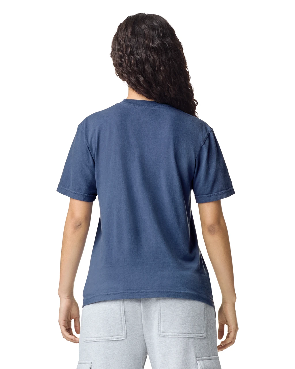 Person viewed from the back, wearing a blue short-sleeve T-shirt and light gray shorts, with dark curly hair around the shoulders