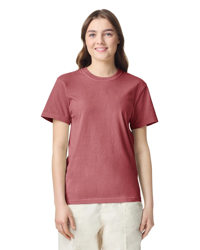 Smiling woman in a dusty rose short-sleeve T-shirt and light beige pants against a white background.