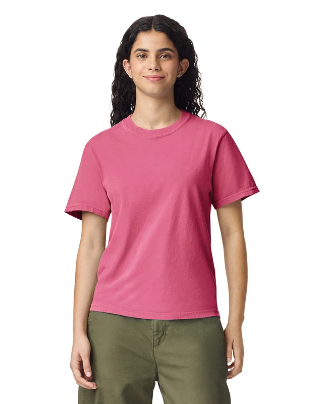Woman wearing a pink t-shirt and olive-green pants, standing and smiling against a white background.