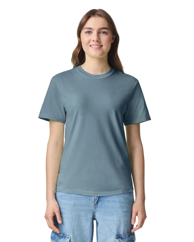 Woman standing and smiling, wearing a blue-gray T-shirt and light jeans, facing the camera against a white background.
