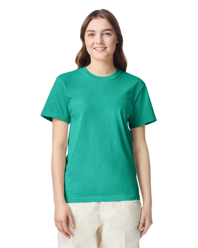 Woman wearing a green T-shirt and light beige pants, smiling at the camera against a white background.