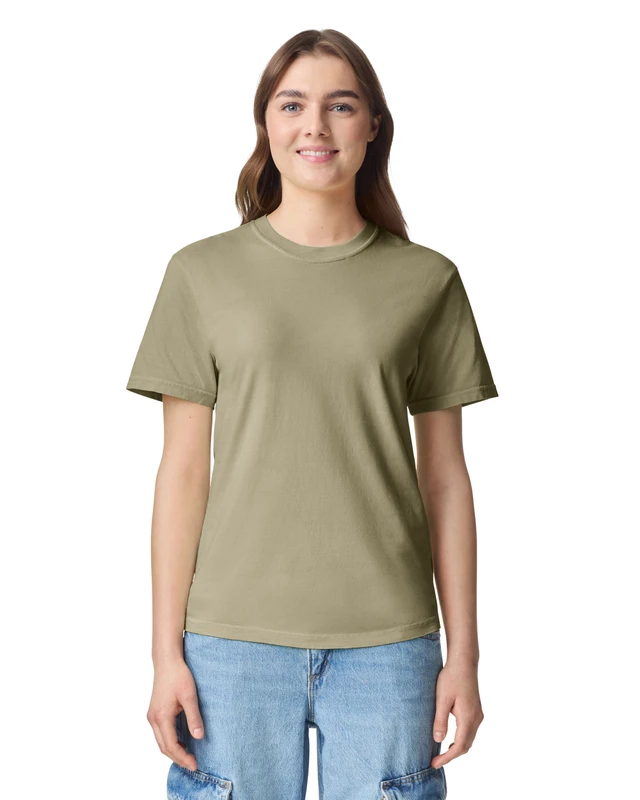 Young woman standing against a white background wearing an olive green t-shirt and light blue jeans, smiling.