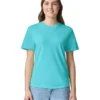 Woman standing, smiling, wearing a turquoise crew-neck T-shirt and light blue jeans against a white background.