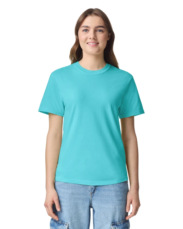 Woman standing, smiling, wearing a turquoise crew-neck T-shirt and light blue jeans against a white background.