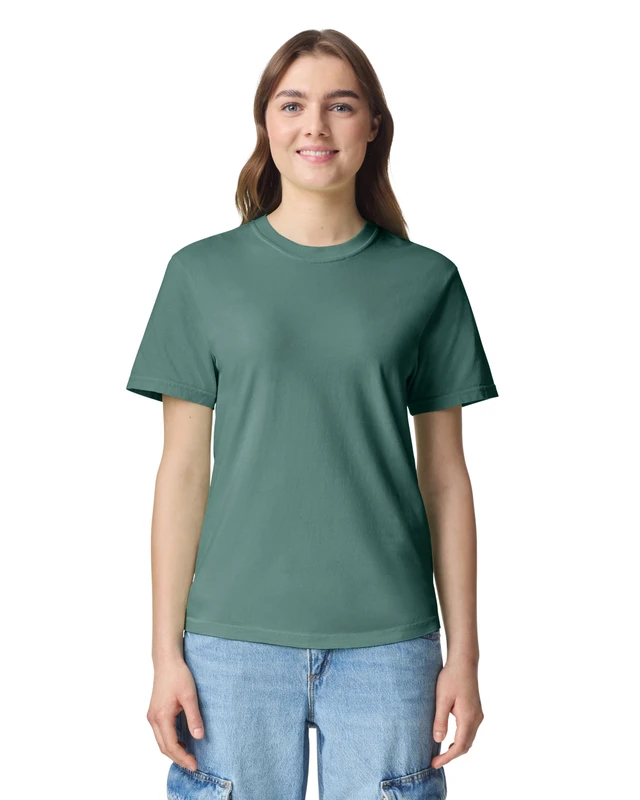 Young woman wearing a teal-green T-shirt and light blue jeans, standing against a white background with a friendly smile.