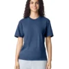 Woman with dark curly hair wearing a navy T-shirt and light gray joggers, standing against a white background, smiling at the camera.