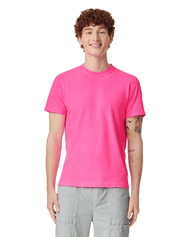 Young man with curly brown hair smiling, wearing a hot pink T-shirt and light gray cargo shorts against a white background.