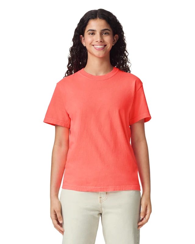 Woman wearing a coral T-shirt and light pants, smiling at the camera against a white background.