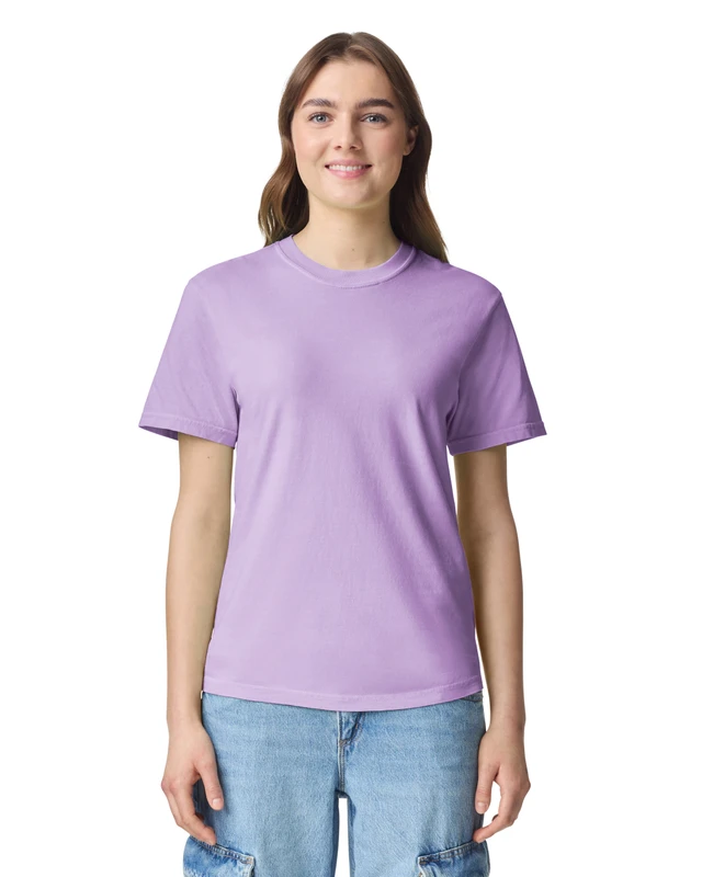 Woman in a lavender T-shirt and blue jeans smiles at the camera against a white background.