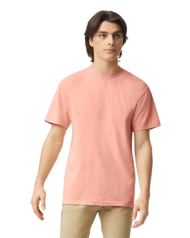 Young man modeling a salmon-pink short-sleeve T-shirt with beige pants, standing and looking off to the side.