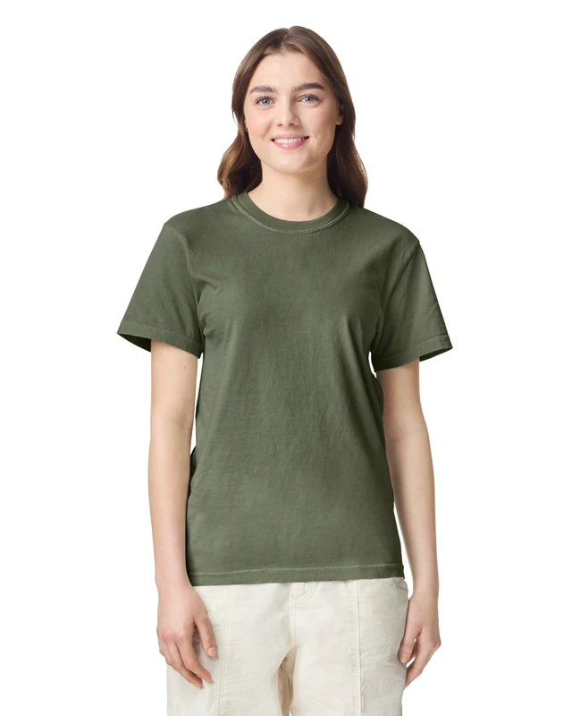 Woman wearing an olive-green crew-neck T-shirt and light beige pants, smiling at the camera on a white background.