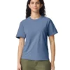 Woman standing and smiling, wearing a blue short-sleeve T-shirt and olive-green pants, against a white background.