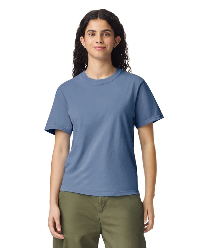 Woman standing and smiling, wearing a blue short-sleeve T-shirt and olive-green pants, against a white background.