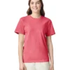 Woman in a coral pink short-sleeve T-shirt facing the camera, smiling, wearing light beige pants in a studio setting.