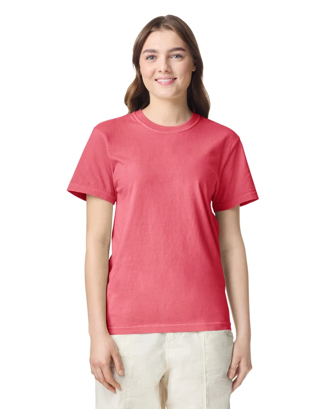 Woman in a coral pink short-sleeve T-shirt facing the camera, smiling, wearing light beige pants in a studio setting.