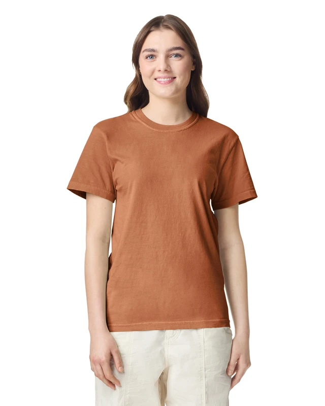 Woman facing the camera, wearing a rust-colored t-shirt and light trousers, smiling warmly.