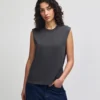 207GD_FadedBlack_05__74348 Woman modeling a dark gray sleeveless top with blue jeans, standing with one hand in her pocket against a light backdrop.