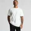 5026G_CLASSIC_ORGANIC_TEE_LOOSE__60124 Man wearing a plain white crew-neck T-shirt and black pants, standing against a light gray background.