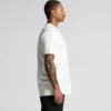 5026G_CLASSIC_ORGANIC_TEE_SIDE__16290 Side profile of a man in a plain white T-shirt, showing a tattooed left arm, against a light gray background.