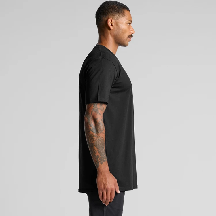 5070_CLASSIC_PLUS_TEE_SIDE__11966 Side profile of a man wearing a black short-sleeve T-shirt, with a tattooed arm, against a gray studio backdrop.