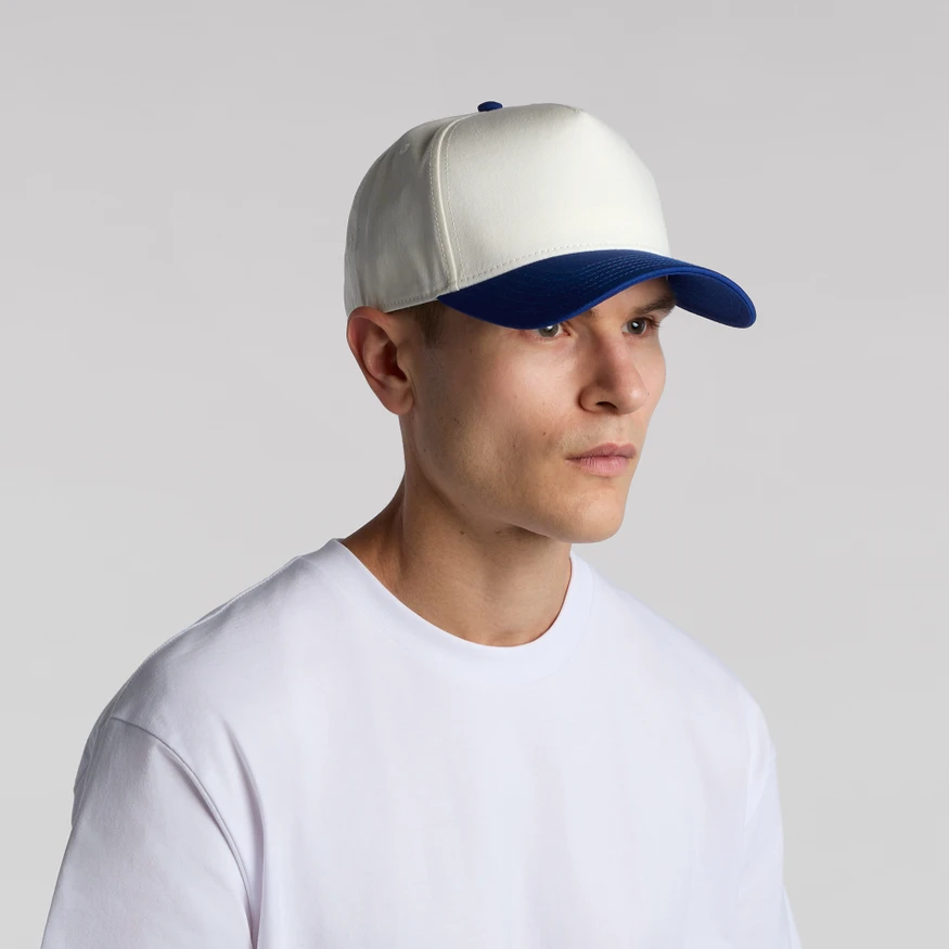 CLASS_2_TONE_MAIN__28616 Portrait of a person wearing a white cap with a blue brim and a white t-shirt, facing slightly to the right against a neutral gray backdrop.