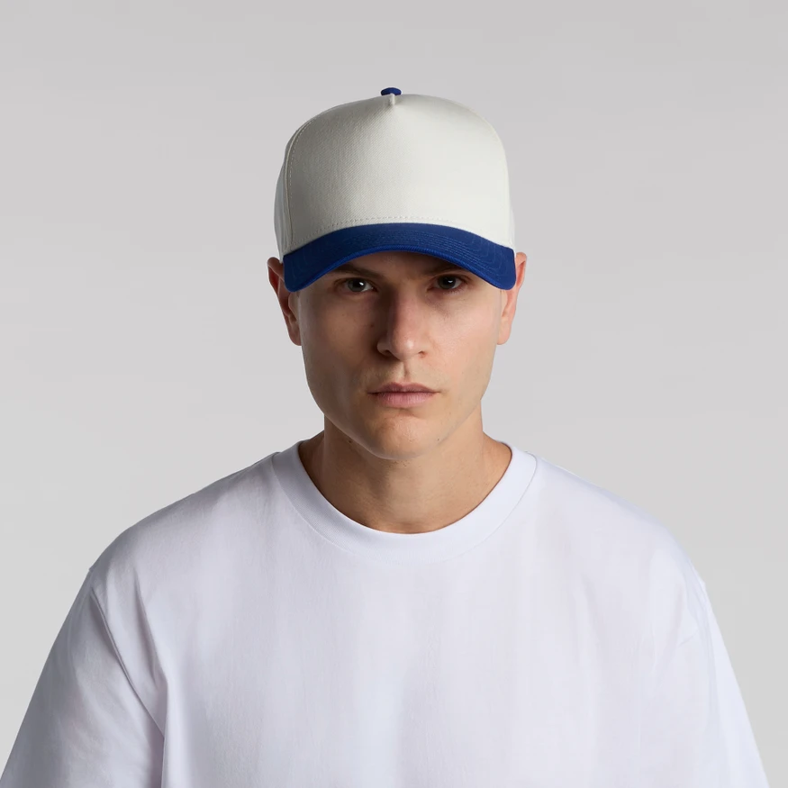 CLASS_2_TONE_TURN__13362 Young man wearing a white baseball cap with a blue brim and a plain white T‑shirt, facing the camera against a light gray background.