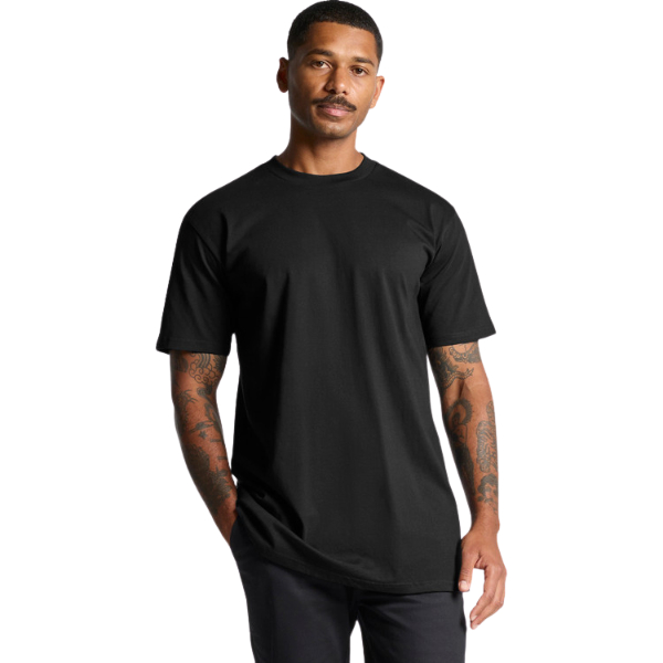 Classic Plus Tee +5cm 5070 Man in a black short-sleeve T-shirt standing with one hand in his pocket, tattoos visible on his arms.